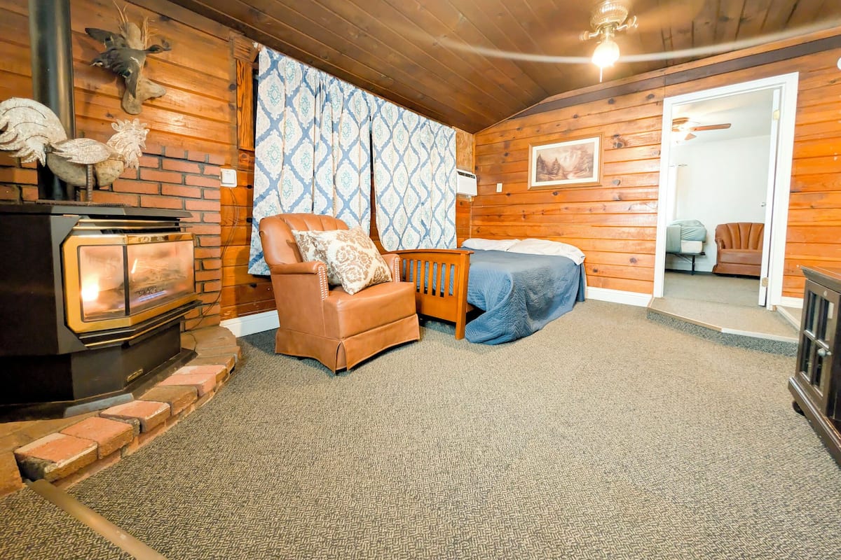 A cozy room with a fireplace, a leather chair, a bed, and a wooden wall.