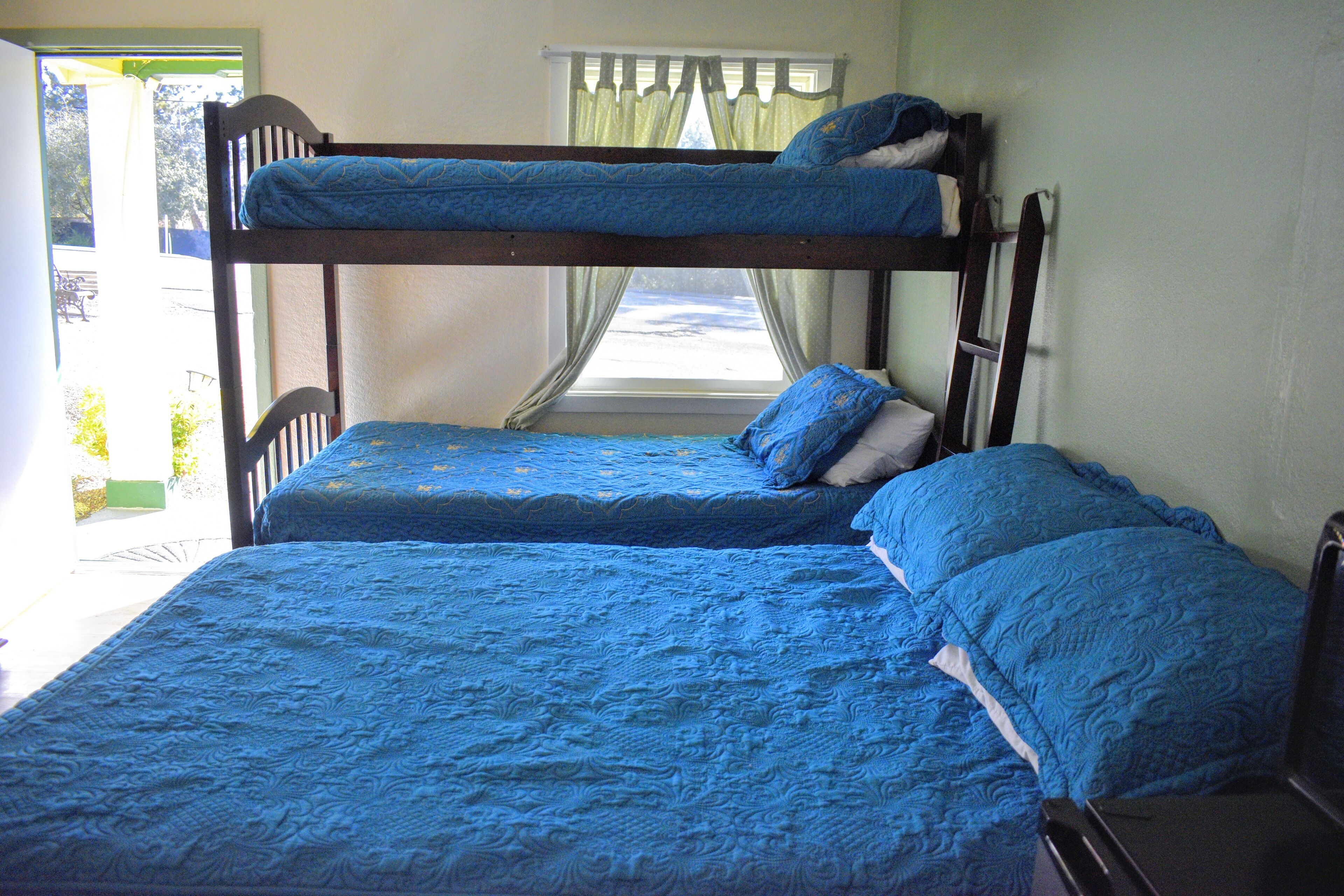 Een stapelbed met blauw beddengoed in een kamer met een raam en gordijnen.