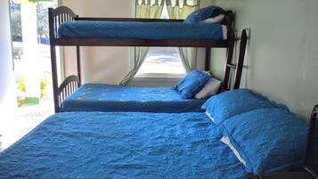 Een stapelbed met blauw beddengoed in een kamer met een raam en gordijnen.