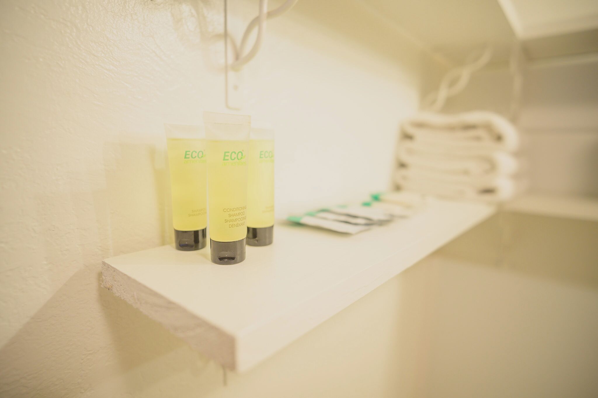 A shelf with three bottles of ECO shampoo and conditioner, and some folded towels in the background.