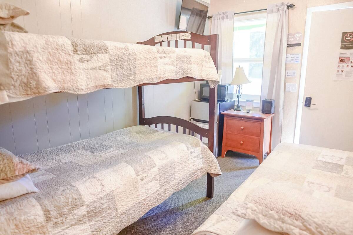 A room with bunk beds, a small bedside table with a lamp, a TV, and a cabinet.