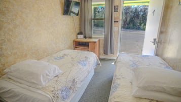 Una habitación con dos camas, una pequeña mesa de madera, un televisor en la pared y una puerta que da al exterior.