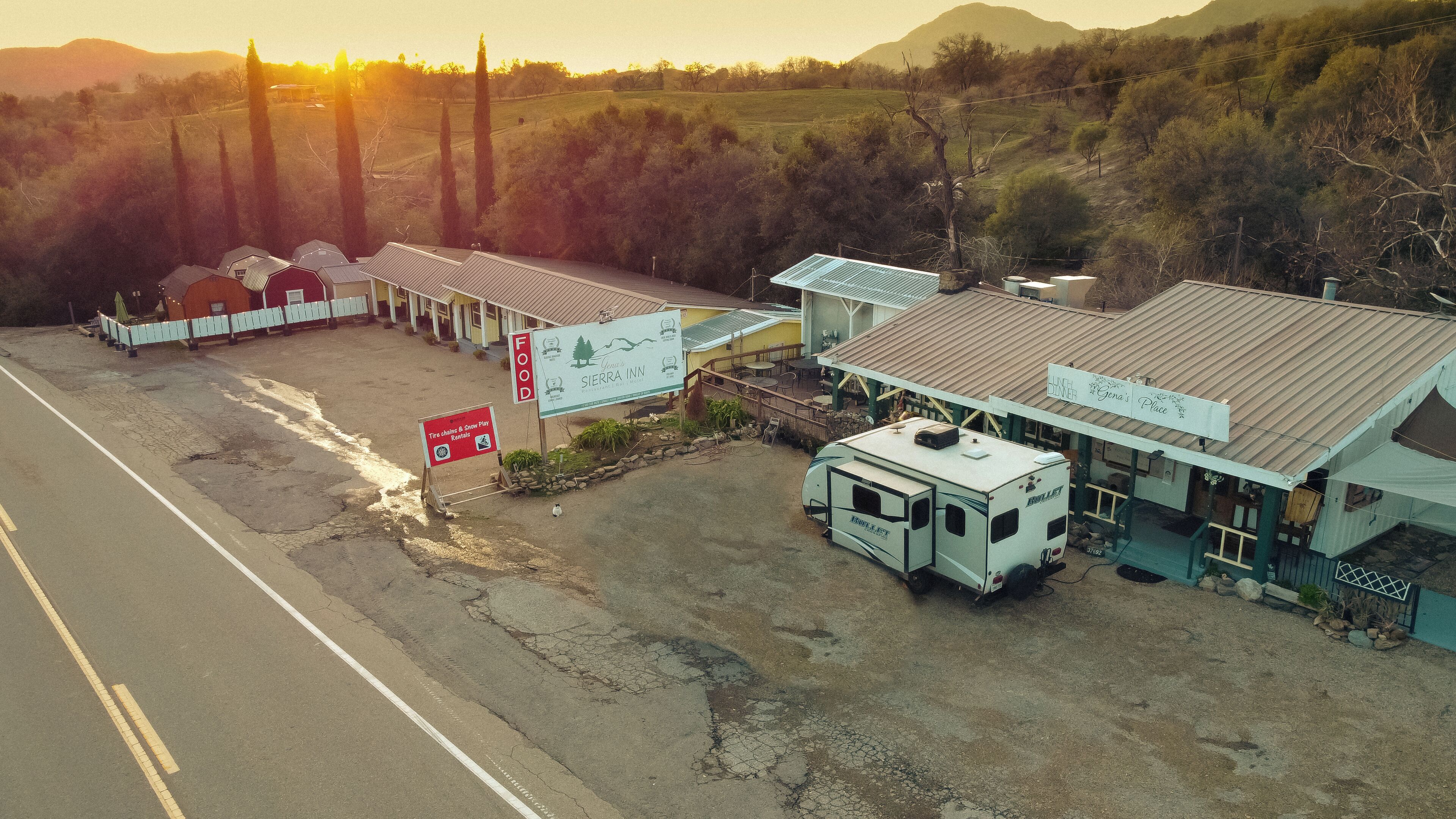 A motel with a dining area, a sign for tire chains & snow play rentals, and a trailer parked in front.
