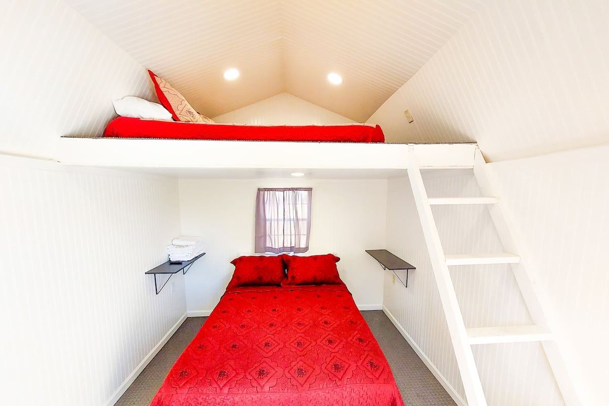 A room with a bunk bed, a desk with a chair, and a ladder.