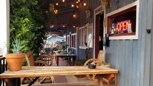 An outdoor seating area with wooden tables and chairs, potted plants, and string lights.