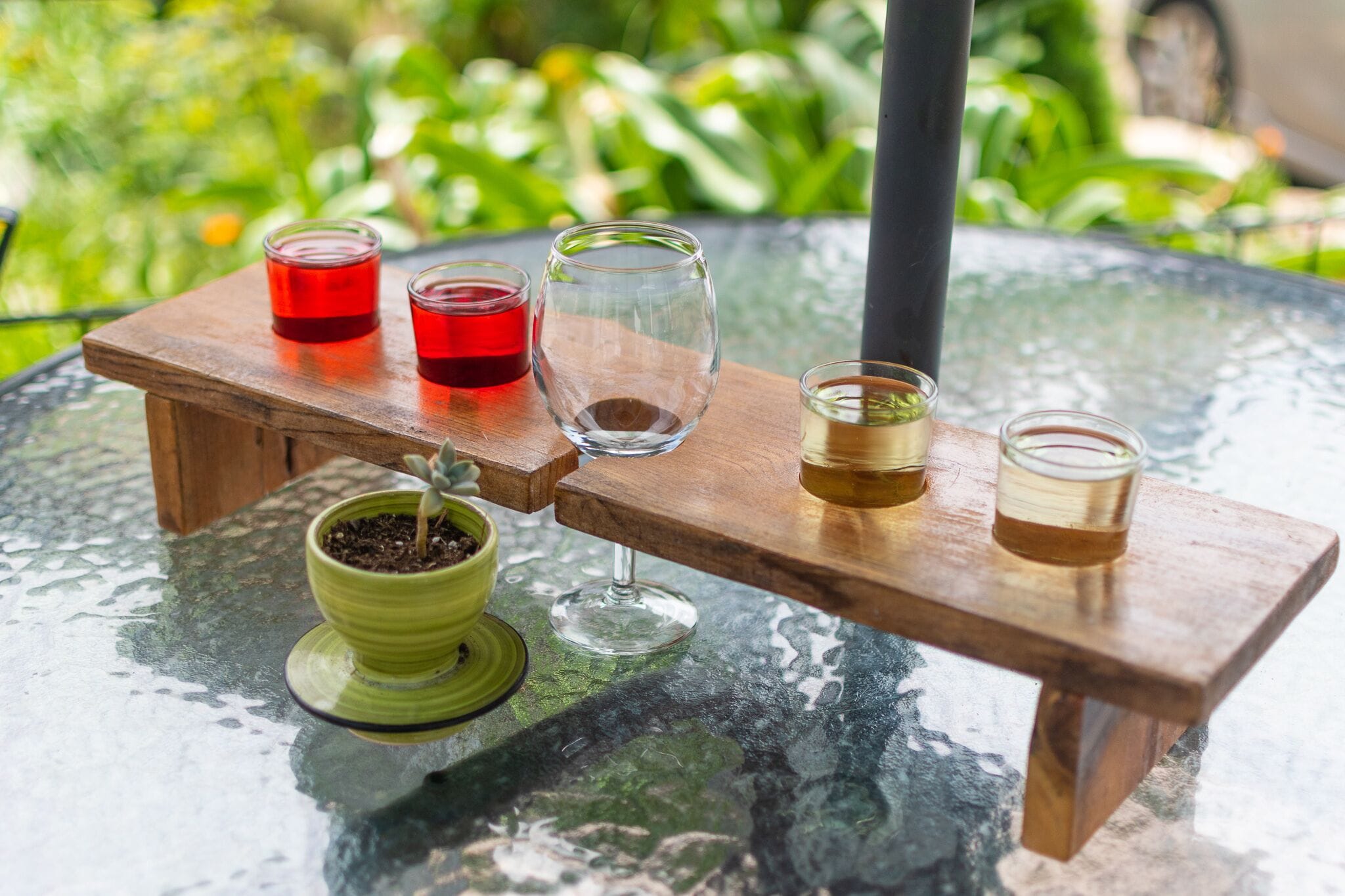 A glass table with a wooden stand holding four glasses and a potted plant.