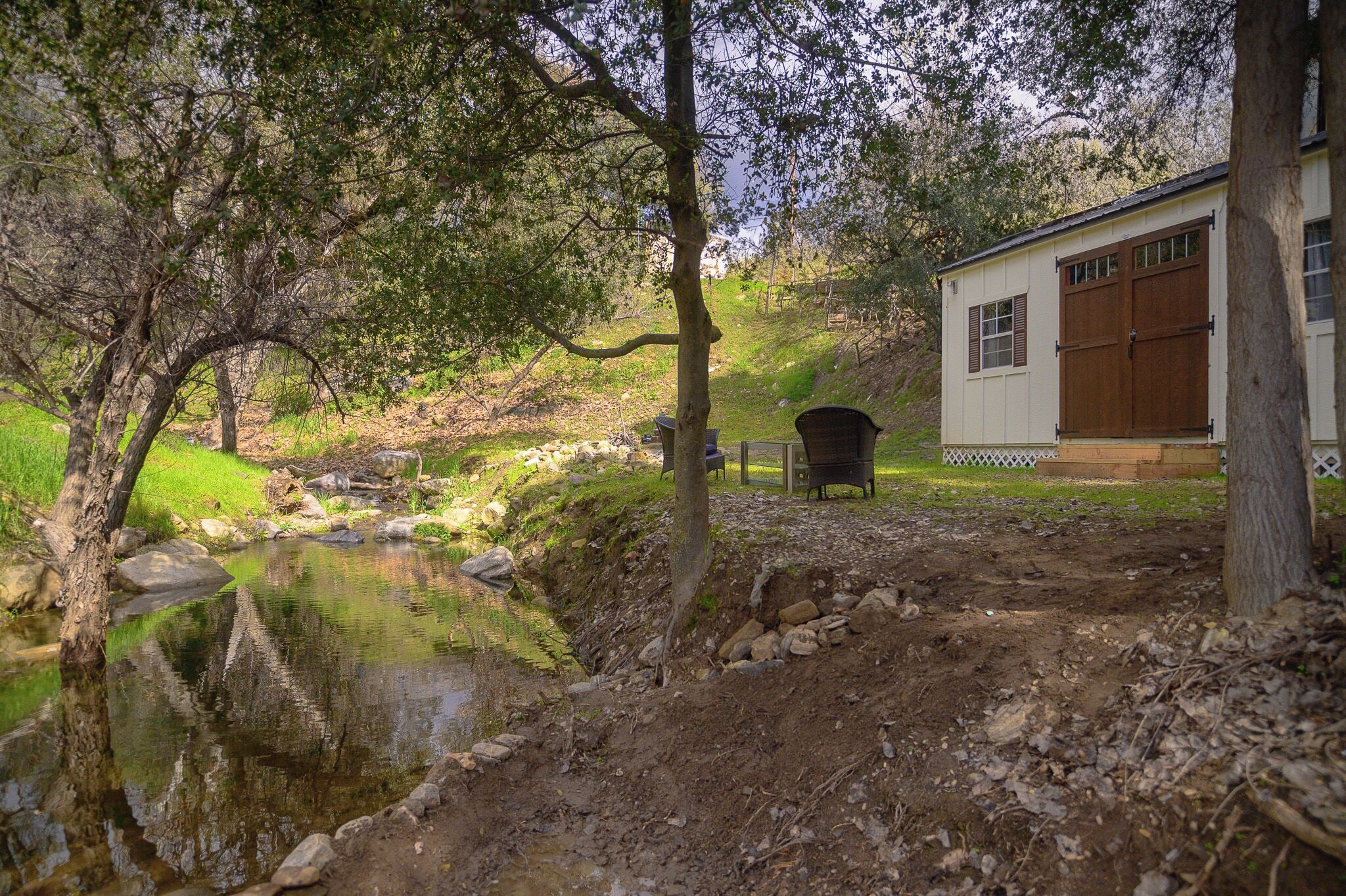 A rustic cabin with a pond, surrounded by trees and a grassy area.