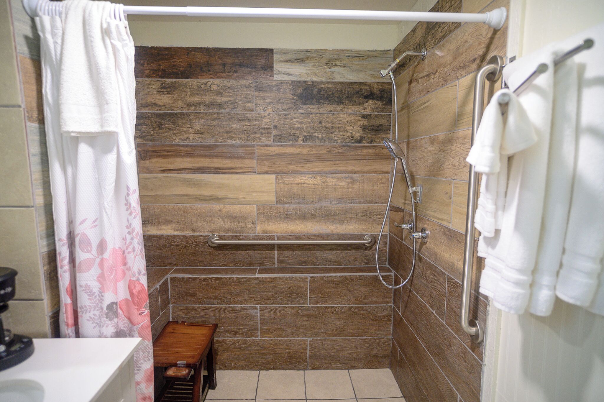 Zona de ducha con pared de madera, barra de apoyo y toallero.