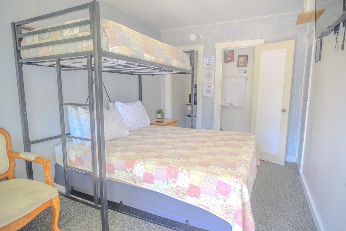 A bunk bed with a quilted bedspread, a wooden chair, and a door with a towel hanging on it.