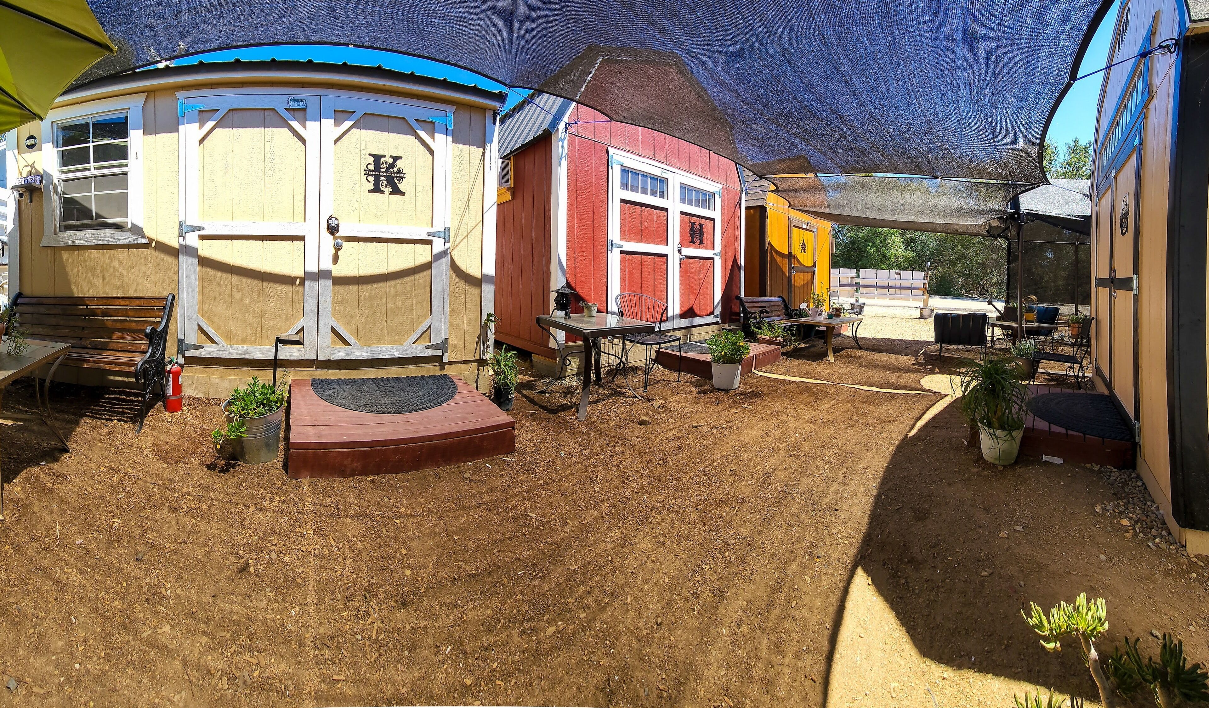 A fenced backyard with a covered patio area, a fire extinguisher, and outdoor seating.