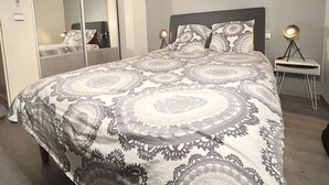 Ein Schlafzimmer mit einem großen Bett, einem Nachttisch, einer Lampe und einem Spiegel.
