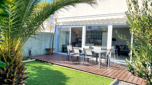 Eine Terrasse mit Tisch und Stühlen, eine Rasenfläche und ein weißes Gebäude mit Glastür.
