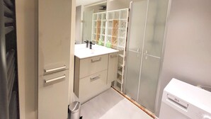 Ein modernes Badezimmer mit großem Spiegel, Waschbecken, Waschtisch, begehbarem Kleiderschrank und Duschbereich.