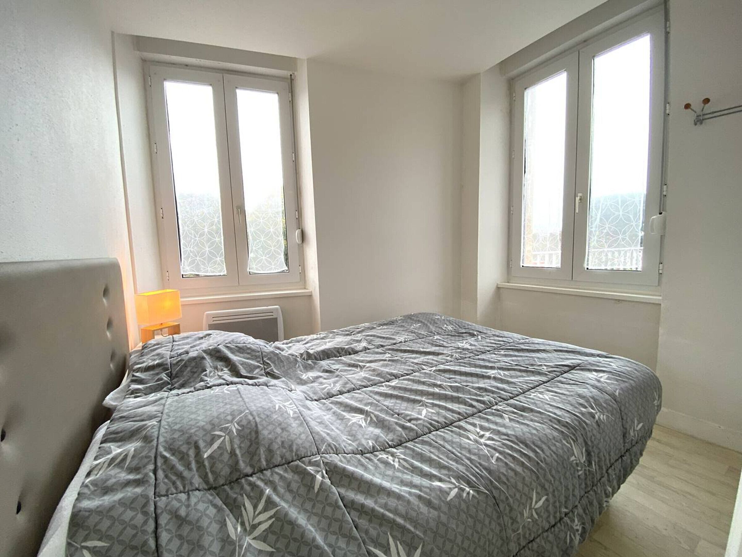A bedroom with a bed, two windows, a radiator, and a lamp.