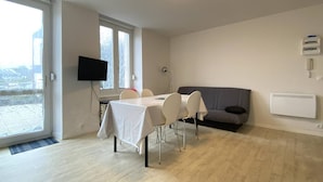 A modern living room with a dining table, chairs, a grey sofa, a flat-screen TV, and a large window. - Cozy Apartment with Free WiFi, Terrace, Near Trestraou Beach in Perros-Guirec (Perros-Guirec)