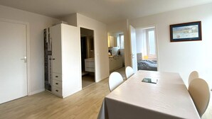 A compact room with a dining table, chairs, a wardrobe, and a small kitchenette. - Cozy Apartment with Free WiFi, Terrace, Near Trestraou Beach in Perros-Guirec (Perros-Guirec)
