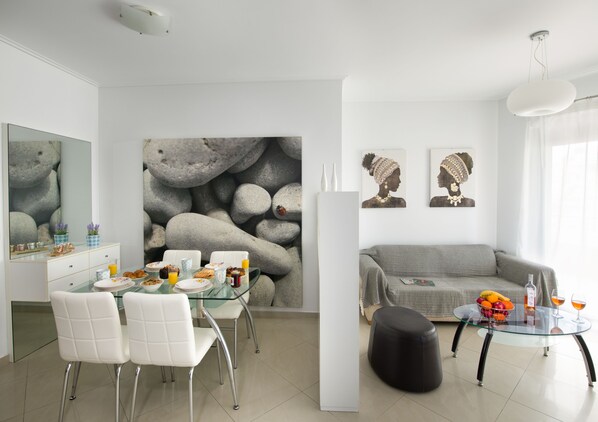 A modern living room with a dining area, a gray sofa, a glass coffee table, and a large rock-themed wall mural.