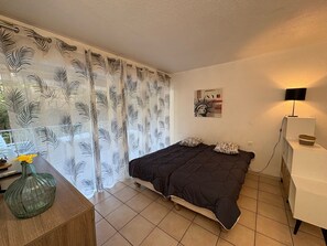 A bedroom with a bed, a nightstand, a lamp, and a wall art piece. - Beachside Studio with AC, Balcony, and Free WiFi - Near Downtown & 50m from the Beach (Saint-Raphaël)
