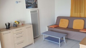 A compact living space with a kitchenette, a sofa with cushions, a small table, and a wall-mounted picture. - Duplex 3-room apartment with pool, air conditioning and garage in Port Camargue (Port Camargue)