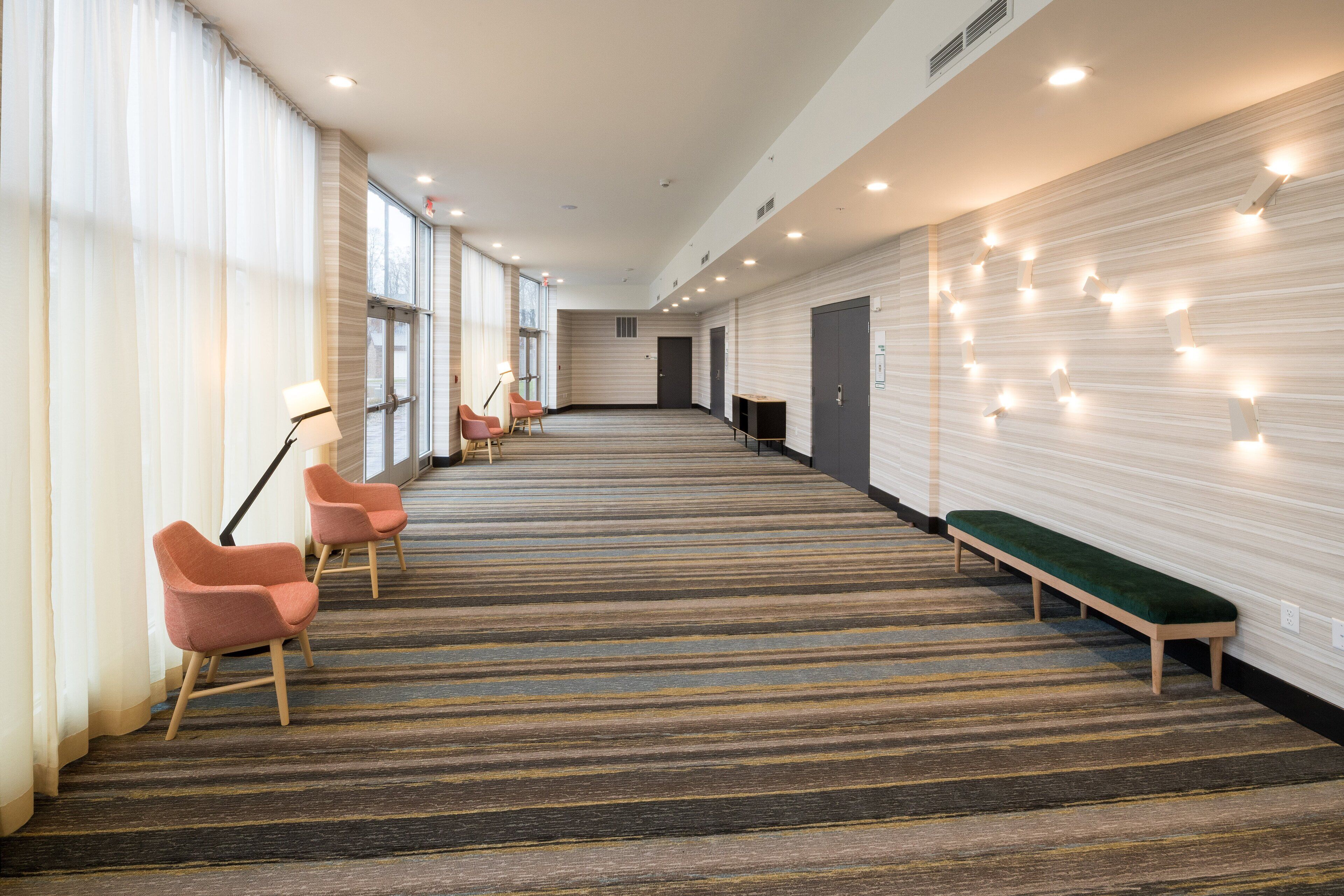 A hotel lobby with a carpeted floor, a green bench, and pink chairs.