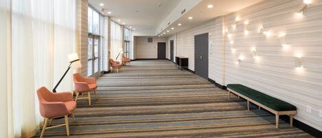 A hotel lobby with a carpeted floor, a green bench, and pink chairs.
