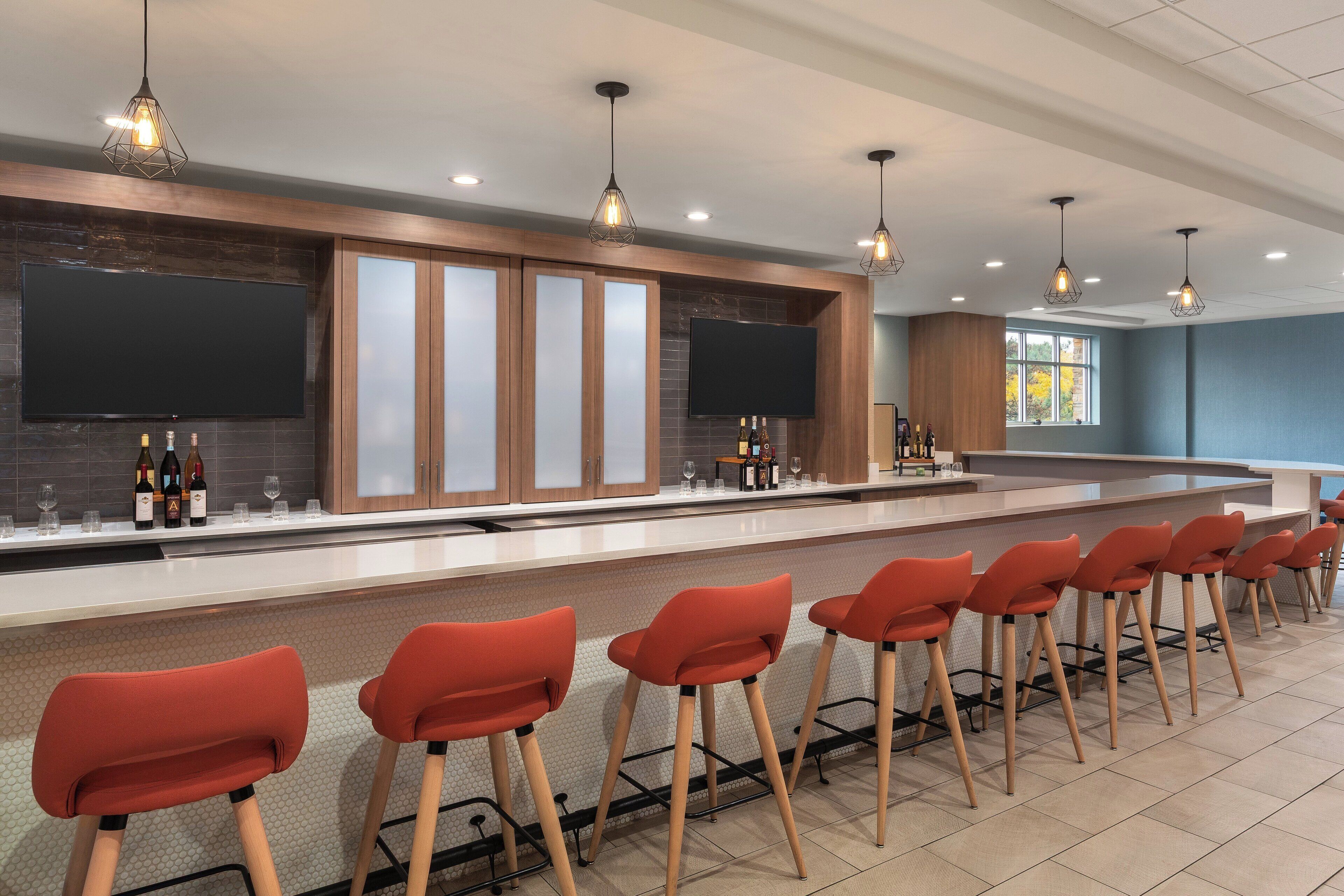 A modern bar area with a long counter, multiple bar stools, and pendant lighting.