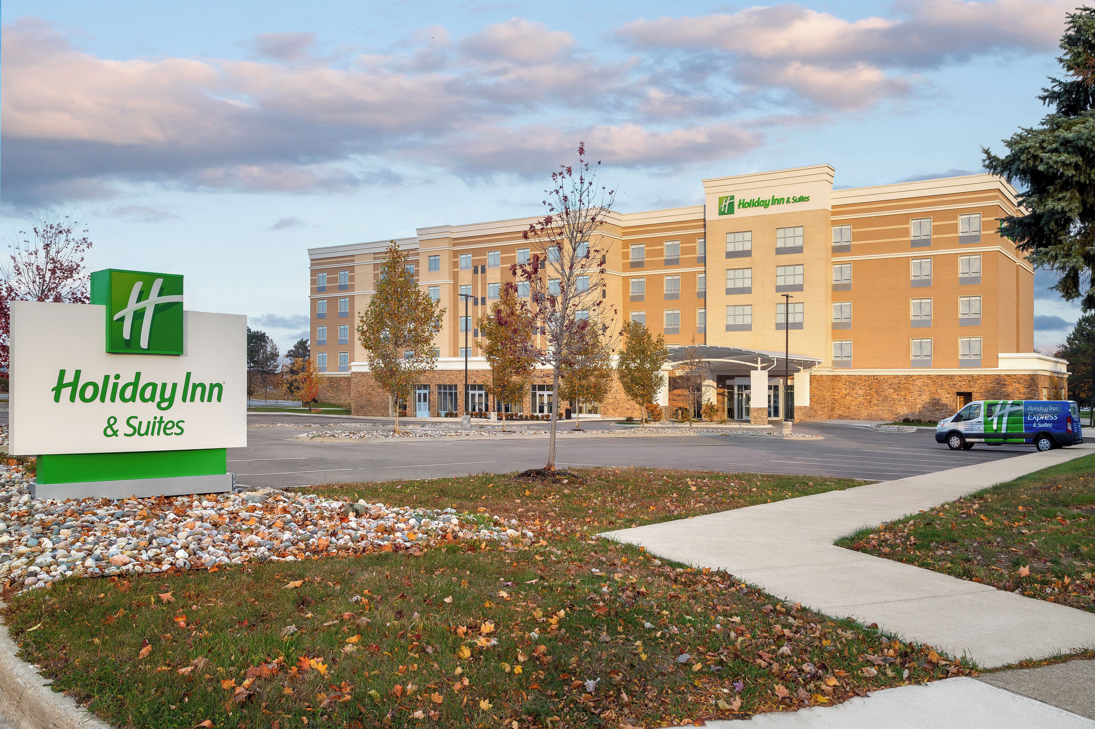 A Holiday Inn & Suites building with a large sign, a parking lot, and a delivery van.