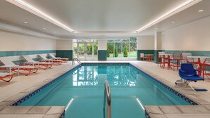 A swimming pool with lounge chairs and tables, surrounded by a tiled deck and a view of greenery. - Holiday Inn & Suites Detroit - Troy by IHG (Troy)