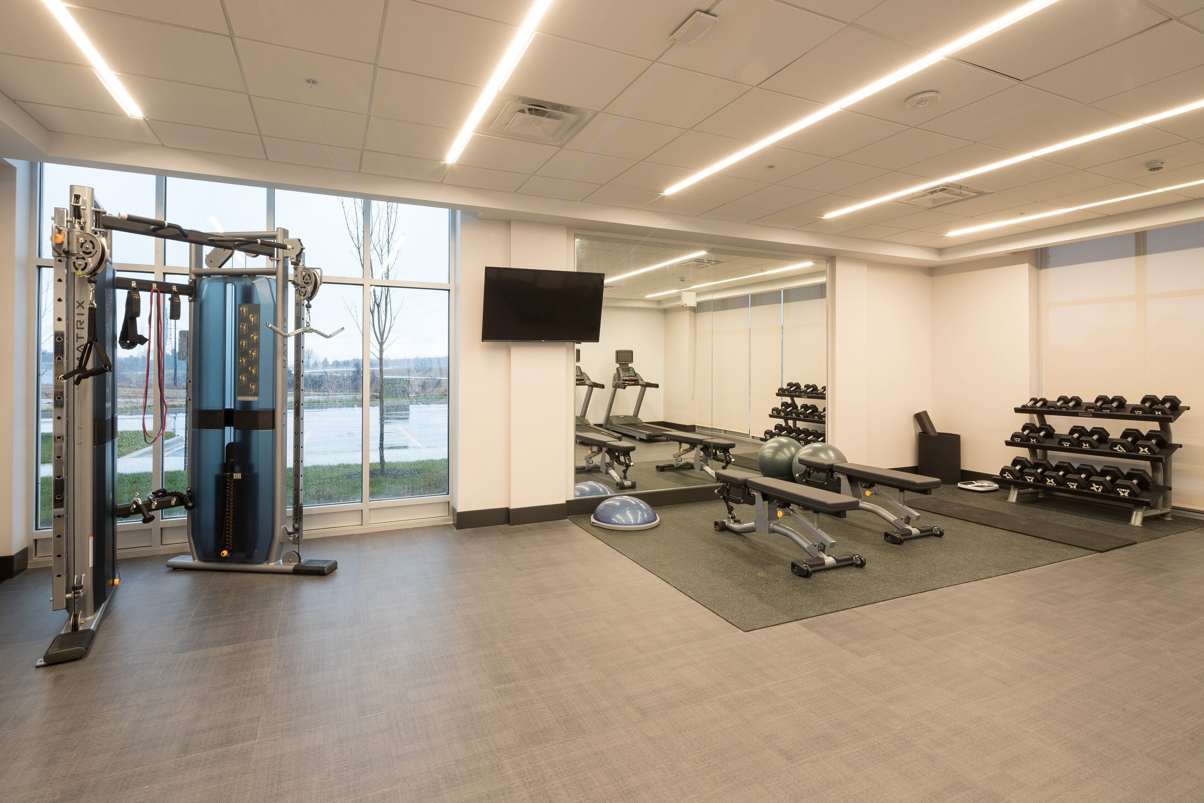 A gym with cardio machines, weightlifting equipment, and dumbbells.