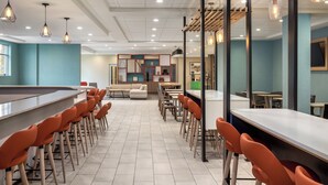 A modern dining area with a long counter and orange chairs, a seating area with sofas, and pendant lighting. - Holiday Inn & Suites Detroit - Troy by IHG (Troy)