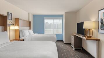 A hotel room with two beds, a desk with a TV, a lamp, and a window with a view.