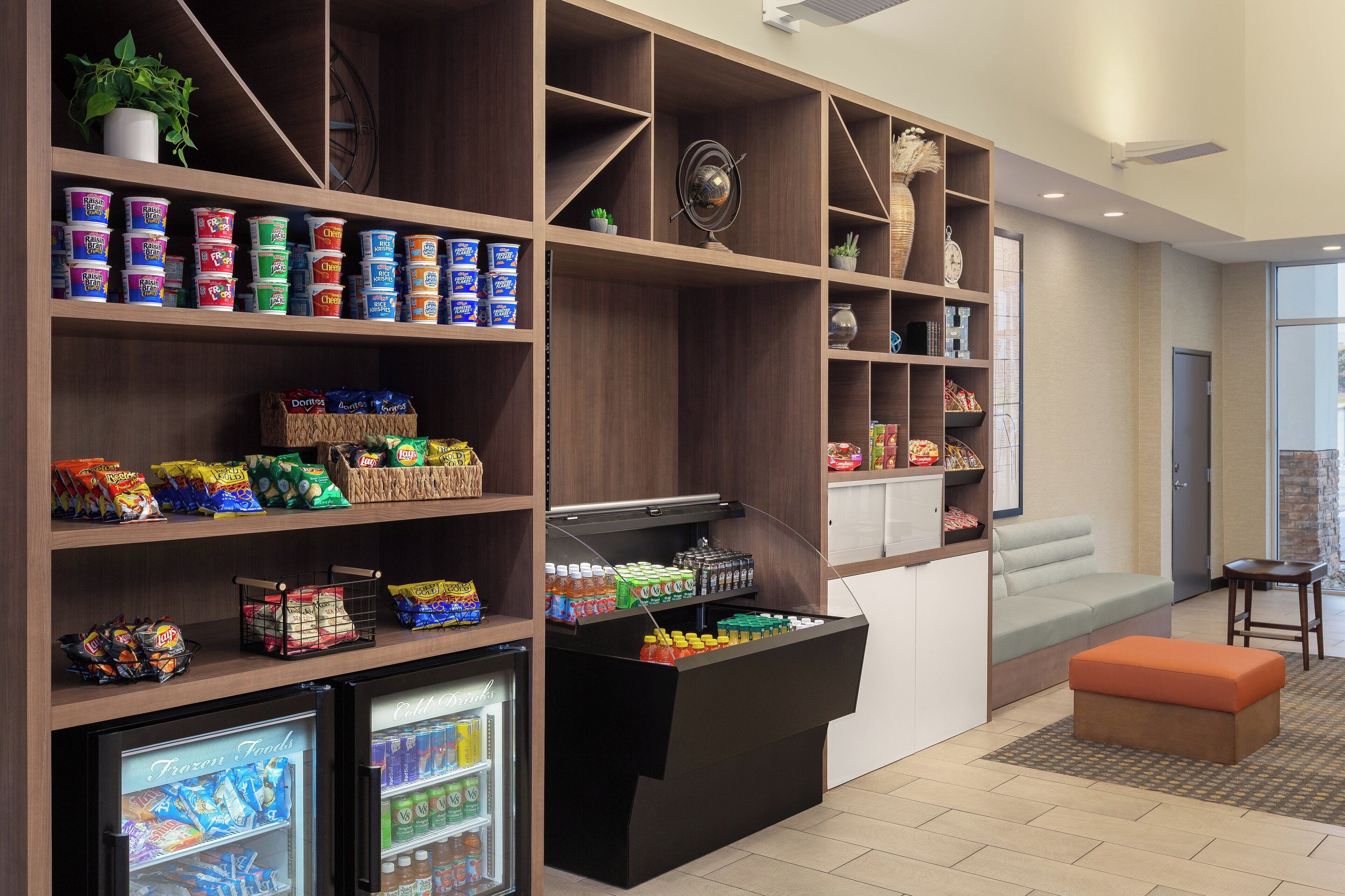 A self-service snack area with refrigerated and freezer sections, a seating area with a sofa and ottoman, and a small table.