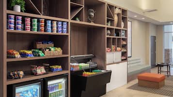 A self-service snack area with refrigerated and freezer sections, a seating area with a sofa and ottoman, and a small table.