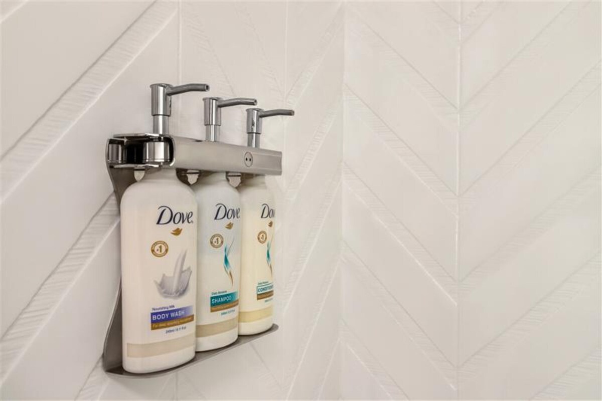 Three Dove body wash bottles mounted on a wall with a geometric tile pattern.
