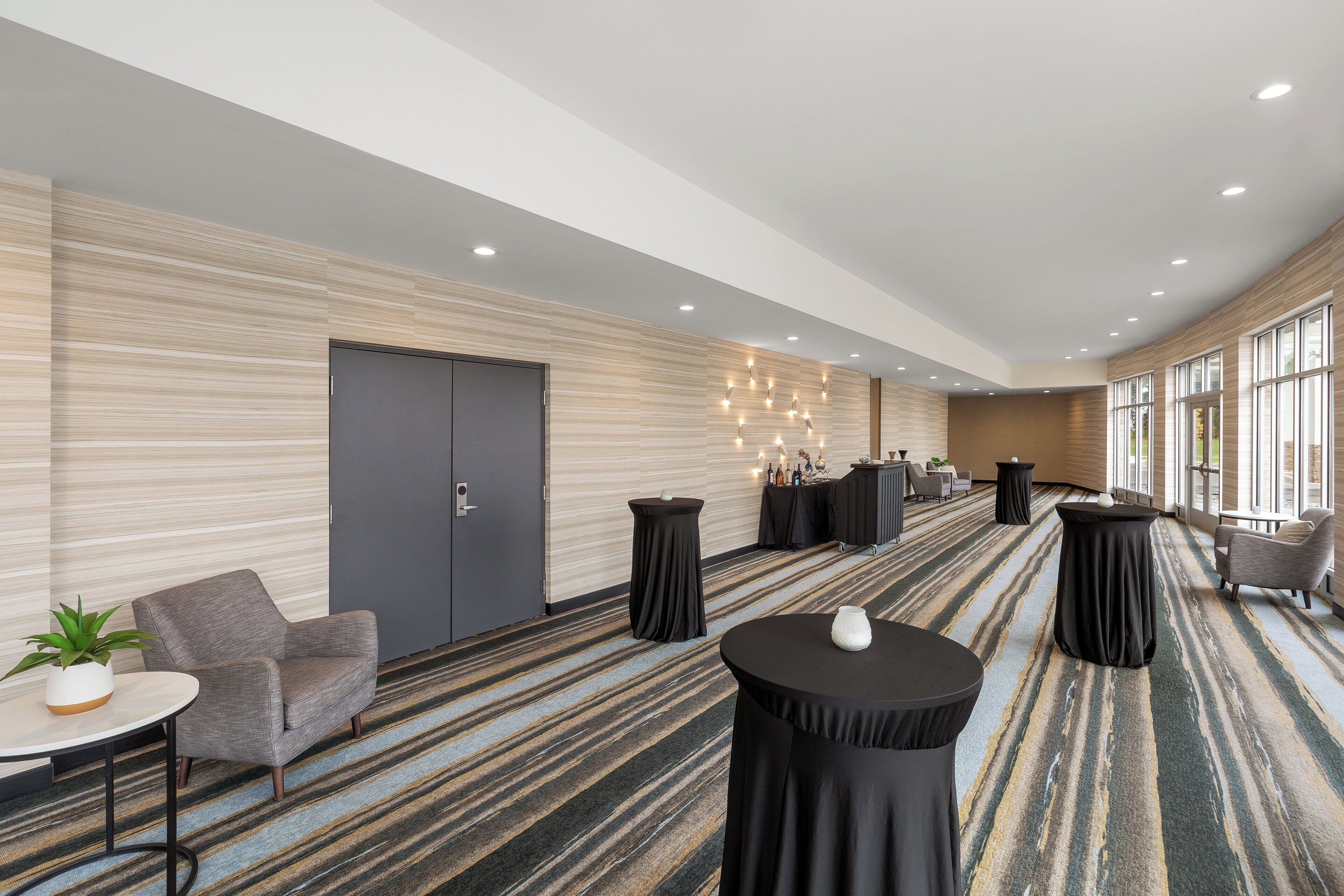 A modern hotel lobby with a striped carpet, seating areas, and a large door.