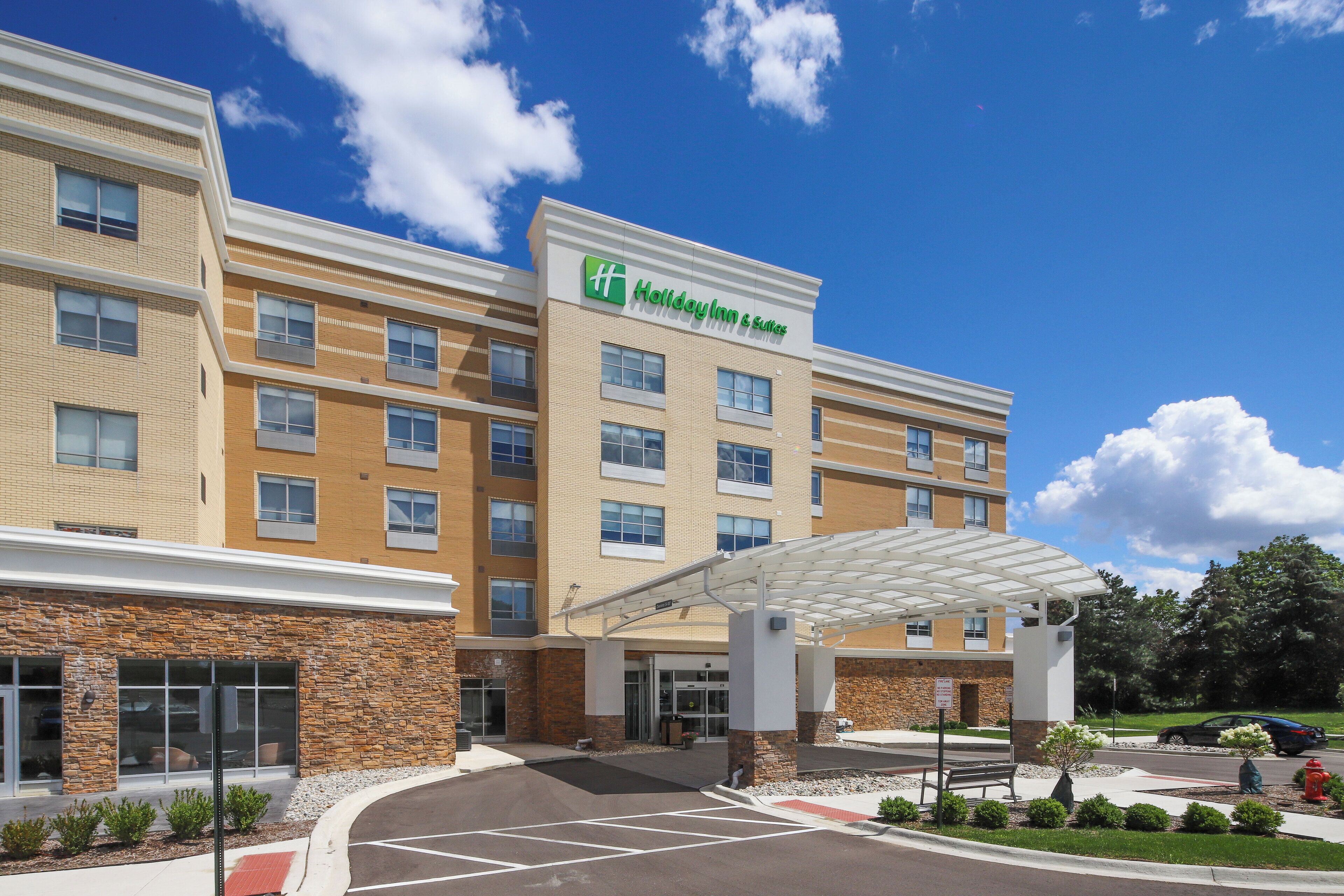 Edificio de Holiday Inn & Suites con entrada cubierta, varias ventanas y un estacionamiento.