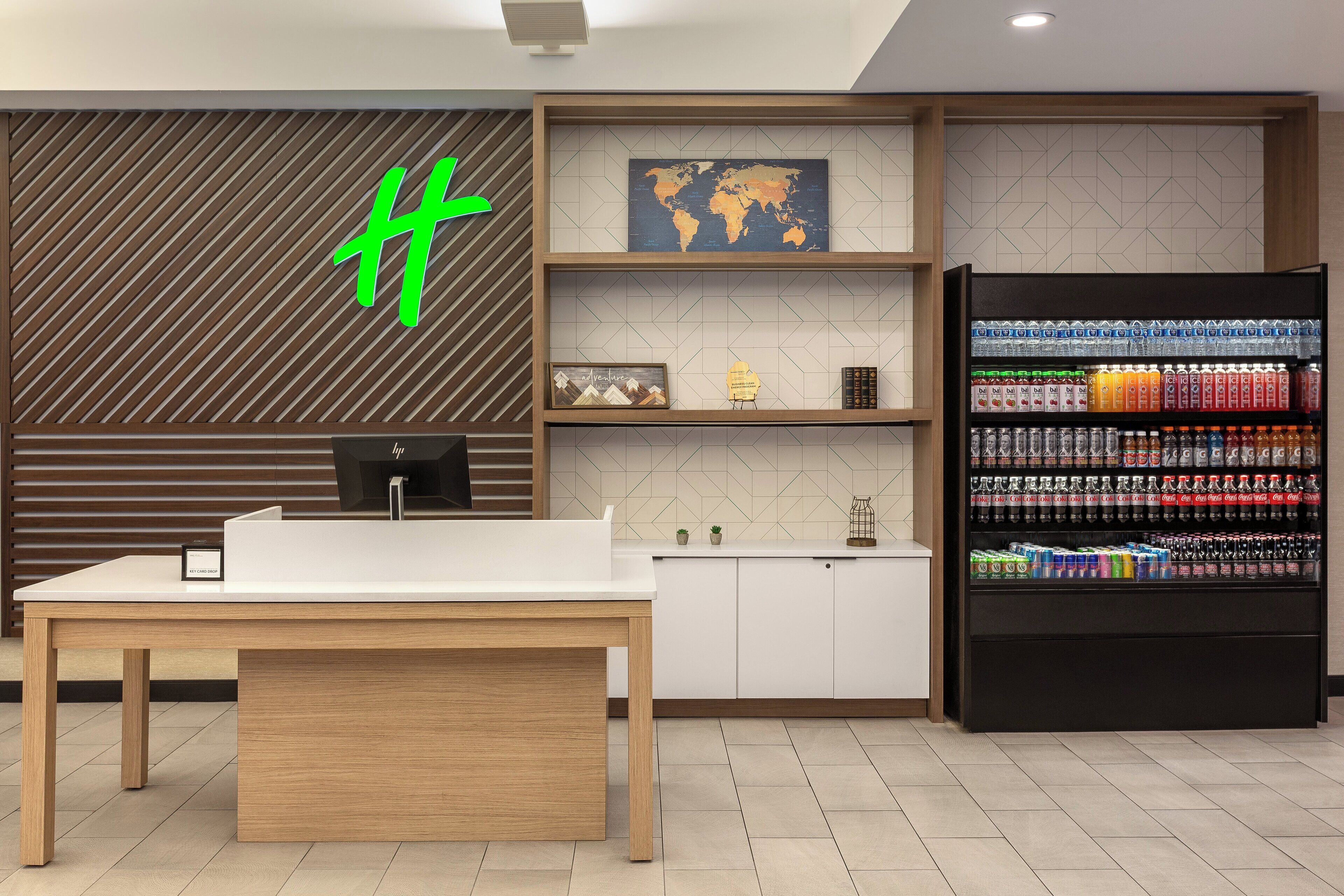 A modern kitchen with a white countertop, wooden cabinets, and a black beverage refrigerator stocked with various drinks.