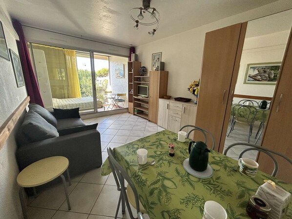 A compact living space with a sofa, dining table, chairs, and a kitchenette.
