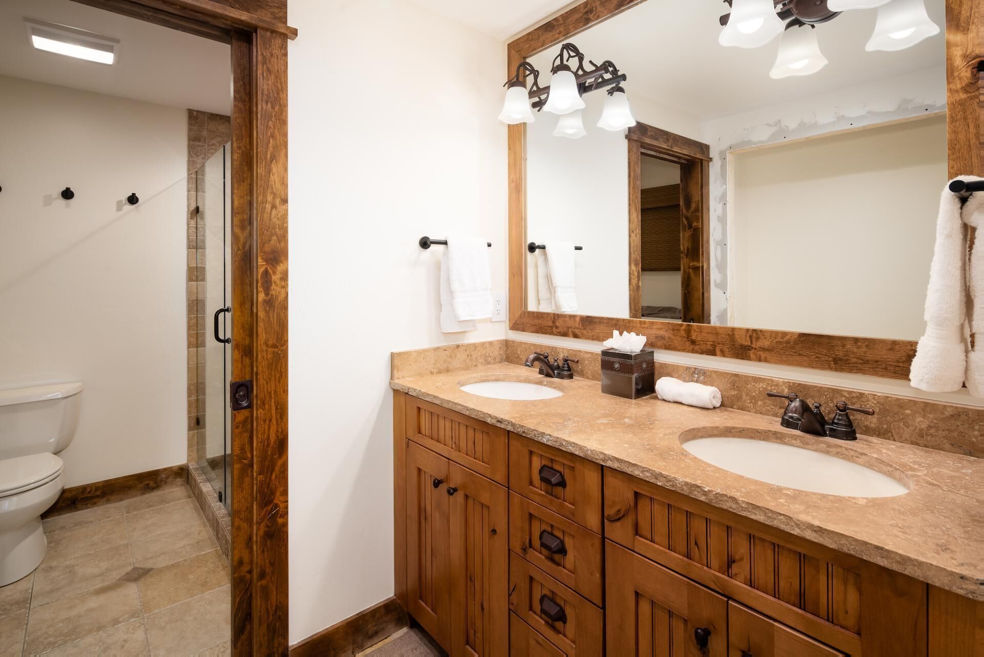 Un baño con muebles de madera, dos lavamanos, un espejo y una zona de ducha.