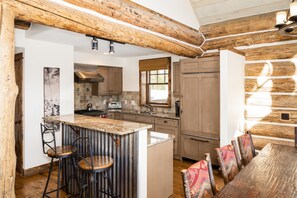 A rustic kitchen with a large island, wooden beams, and a dining area with colorful chairs.