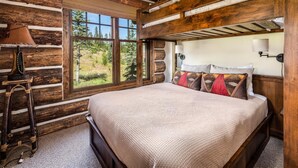 Un dormitori de cabana de fusta amb un llit gran, una finestra amb vista a arbres i una escala de fusta.