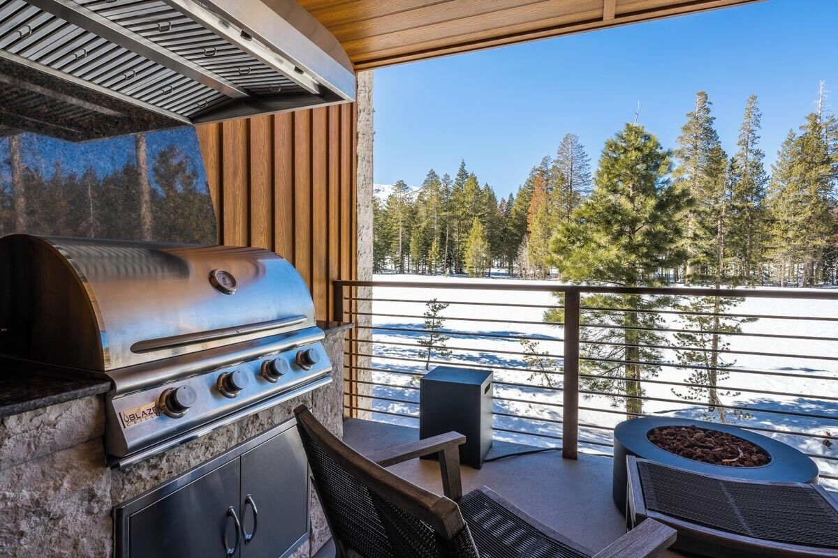 A modern outdoor kitchen with a built-in grill, a seating area, and a view of a snowy landscape with trees.