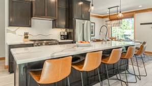 A modern kitchen with dark cabinets, a large island with bar stools, stainless steel appliances, and pendant lighting. - Luxury Mammoth Townhome w/ Hot Tub and Fire Pit (Mammoth Lakes)