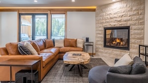 A modern living room with a leather sofa, a wooden coffee table, and a stone wall fireplace. - Luxury Mammoth Townhome w/ Hot Tub and Fire Pit (Mammoth Lakes)