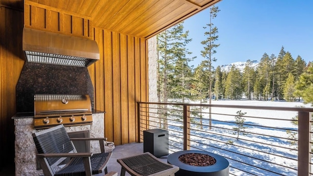 A wooden deck with a stone fireplace, outdoor seating, and a view of a snowy landscape. - Luxury Mammoth Townhome w/ Hot Tub and Fire Pit (Mammoth Lakes)