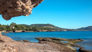 A coastal landscape with rocky terrain, clear blue water, and distant hills.