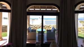 A room with a view of a rocky landscape and the sea. There are two wicker sofas and a small table. - 3 Bedroom Villa in Alghero (Alghero)
