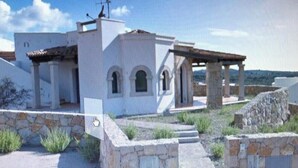 A white building with a stone facade, a covered patio, and a stone wall. - 3 Bedroom Villa in Alghero (Alghero)