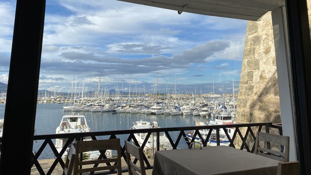 A balcony with a view of a marina filled with boats, a stone wall, and a table with chairs. - 3 Bedroom Villa in Alghero (Alghero)