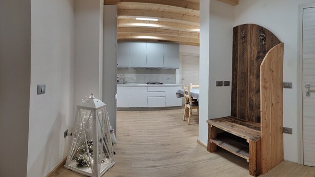 A narrow hallway with a wooden bench, a small table with a glass enclosure, and a kitchen area in the background.